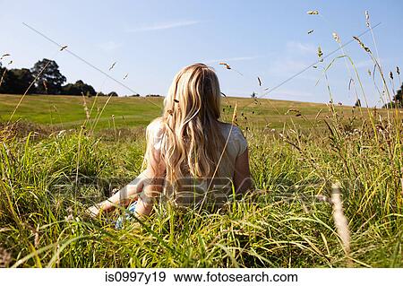 Young woman sitting in a field with back to camera View Large Photo Image Stock Photo - Young woman sitting in a field with back to camera. Fotosearch