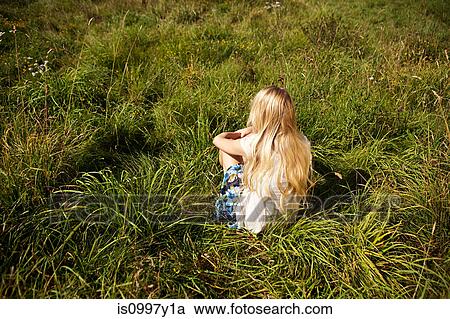 Stock Image - Young woman sitting peacefully in a field. Fotosearch