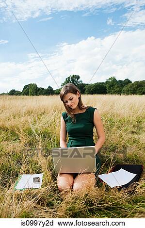 Stock Image - Young woman using a laptop computer in the middle of a field. Fotosearch