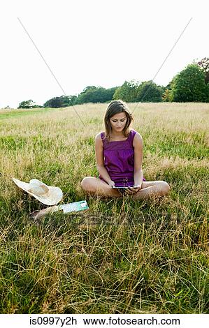 Stock Image - Young woman using hand held device in the middle of a field. Fotosearch