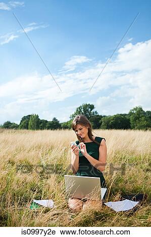 Young woman using laptop and mobile phone in the middle of a field View Large Photo Image Stock Image - Young woman using laptop and mobile phone in the middle of a field. Fotosearch