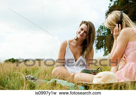 Young woman with headphones on sitting in a field with a friend View Large Photo Image Stock Photo - Young woman with headphones on sitting in a field with a friend. Fotosearch