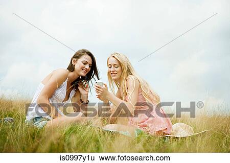 Young women looking at a hand held device together View Large Photo Image Stock Photograph - Young women looking at a hand held device together. Fotosearch