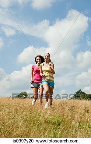 Young women running through a field View Large Photo Image Stock Image - Young women running through a field. Fotosearch