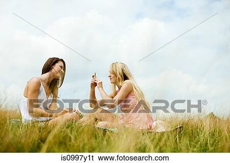 Young women sitting in a field taking a photograph View Large Photo Image Stock Photograph - Young women sitting in a field taking a photograph. Fotosearch