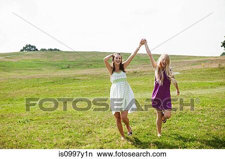 Young women skipping through field with arms raised and hands held View Large Photo Image Picture - Young women skipping through field with arms raised and hands held. Fotosearch