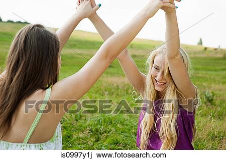 Stock Image - Young women with arms raised and hands held. Fotosearch