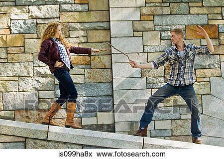 Couple play fighting with sticks against stone wall View Large Photo Image Stock Photo - Couple play fighting with sticks against stone wall. Fotosearch