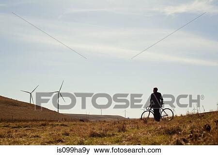 Stock Photo - Distant view of man by bicycle watching wind farm. Fotosearch