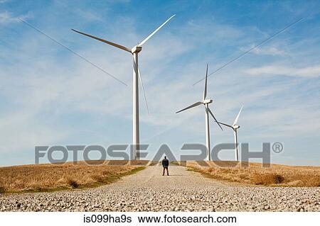 Stock Photograph - Distant view of man in front of wind turbines. Fotosearch