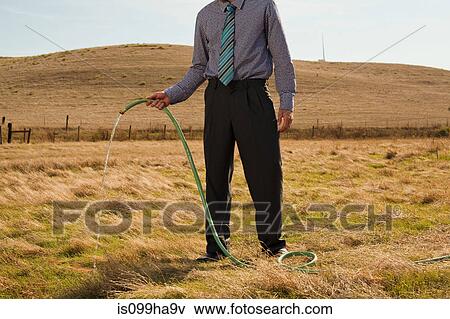 Man holding hose pipe in arid landscape View Large Photo Image Stock Photo - Man holding hose pipe in arid landscape. Fotosearch