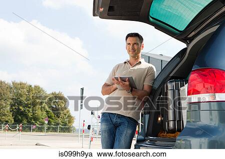 Stock Image - Man using data tablet in airport carpark. Fotosearch