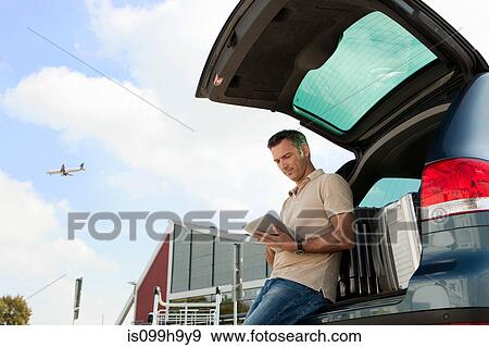 Man using data tablet in airport carpark View Large Photo Image Stock Photo - Man using data tablet in airport carpark. Fotosearch