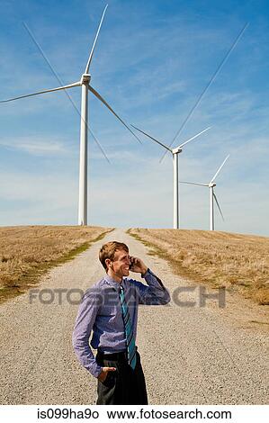 Man using mobile phone in front of wind turbines View Large Photo Image Picture - Man using mobile phone in front of wind turbines. Fotosearch