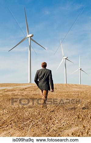 Stock Photography - Man walking in front of wind turbines. Fotosearch