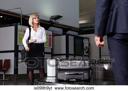 Stock Photograph - Mid adult businesswoman waiting for luggage in airport baggage re-claim. Fotosearch