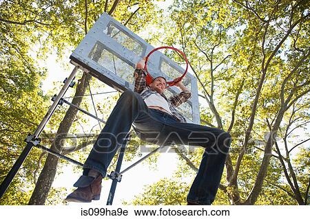Stock Image - Mid adult man hanging from basketball hoop. Fotosearch