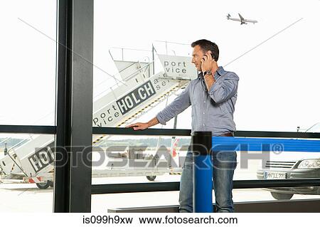 Stock Photo - Mid adult man on the phone at airport viewing platform. Fotosearch