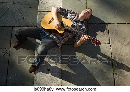 Stock Photo - Mid adult man playing guitar on ground. Fotosearch