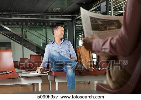 Stock Photo - Mid adult man sitting in airport departure lounge. Fotosearch