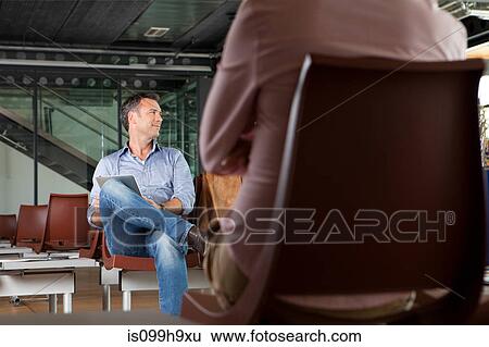 Stock Photograph - Mid adult man sitting in airport departure lounge. Fotosearch