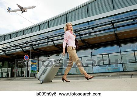 Stock Photograph - Mid adult woman pulling luggage to airport. Fotosearch