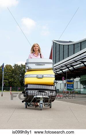 Mid adult woman pushing luggage trolley to airport View Large Photo Image Stock Image - Mid adult woman pushing luggage trolley to airport. Fotosearch