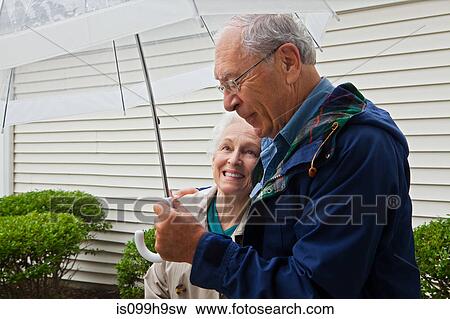 Senior couple holding umbrella outside View Large Photo Image Stock Photo - Senior couple holding umbrella outside. Fotosearch