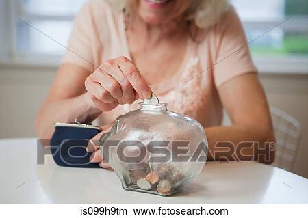 Picture - Senior woman saving money in piggy bank. Fotosearch