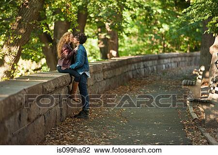 Young couple embracing on wall in park View Large Photo Image Stock Image - Young couple embracing on wall in park. Fotosearch
