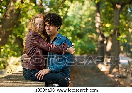 Stock Image - Young couple embracing on wall in park. Fotosearch