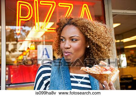 Stock Photo - Young woman eating pizza slice. Fotosearch