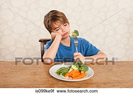 Stock Image - Boy frowning at vegetables. Fotosearch