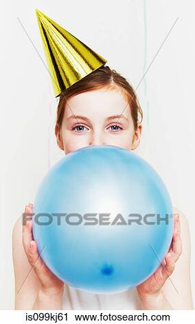 Stock Image - Girl in party hat, blowing up balloon. Fotosearch