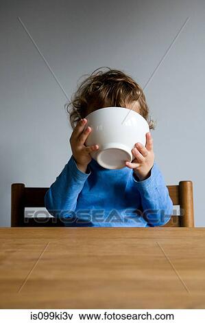 Stock Photo - Little boy holding bowl to his face. Fotosearch