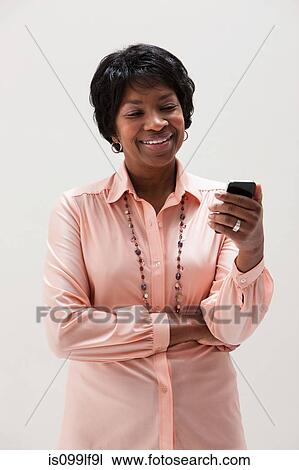 Stock Image - African American mature woman using cellphone, studio shot. Fotosearch