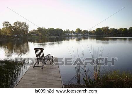 Stock Image - Deck chair on jetty by lake. Fotosearch
