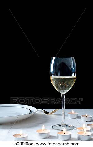 Stock Image - Glass of white wine and tea lights on table. Fotosearch