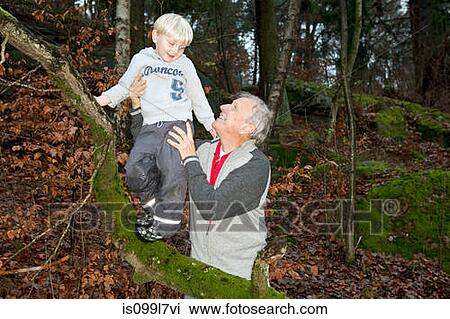 Stock Image - Grandfather holding boy on tree branch. Fotosearch