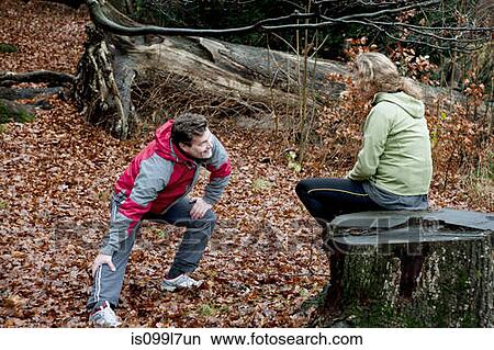 Picture - Mature couple performing warming up exercises in forest. Fotosearch