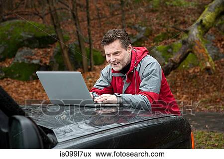 Stock Photo - Mature man using laptop on car bonnet. Fotosearch