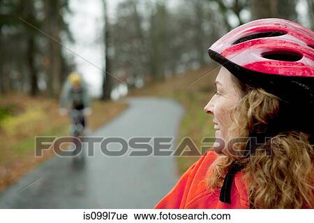 Stock Image - Mature woman on cycle ride looking over shoulder. Fotosearch