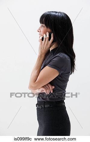Stock Image - Mature woman smiling and using cellphone, studio shot. Fotosearch