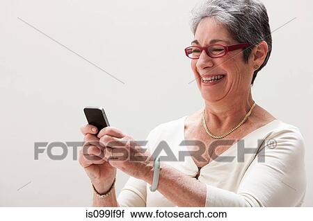 Stock Image - Mature woman smiling and using cellphone, studio shot. Fotosearch