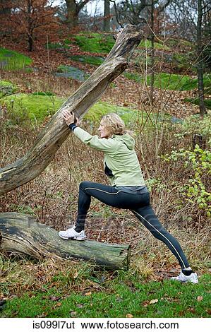 Stock Photograph - Mature woman stretching against tree in forest. Fotosearch