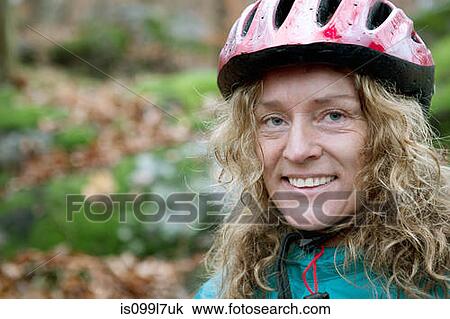 Stock Image - Mature woman wearing cycling helmet in forest. Fotosearch