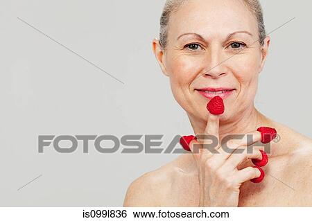 Stock Photograph - Mature woman wearing raspberries on fingertips, smiling. Fotosearch