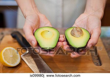 Mid adult woman holding sliced avocado View Large Photo Image Stock Image - Mid adult woman holding sliced avocado. Fotosearch