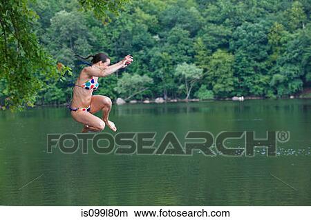 Picture - Mid adult woman leaping into river. Fotosearch