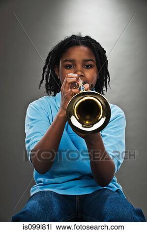 Stock Image - Portrait of black teenage boy playing trumpet, studio shot. Fotosearch